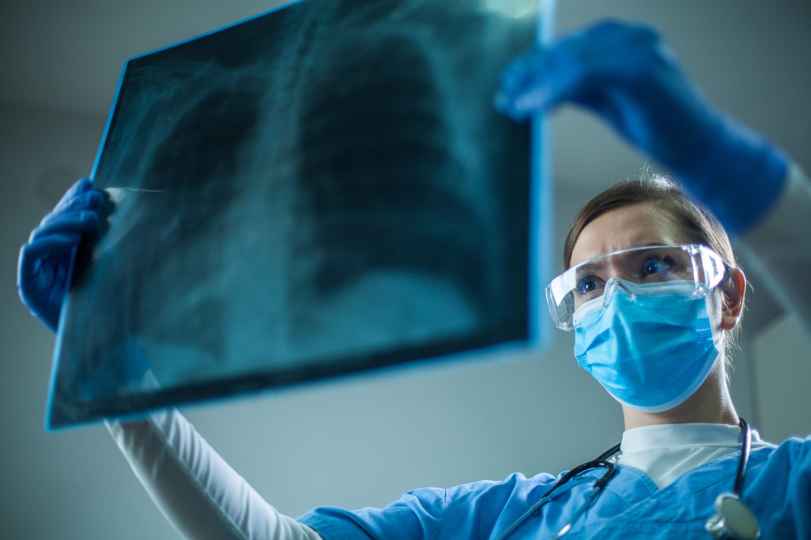 Female pulmonologist or oncologist holding chest X-ray scan,inspecting COVID-19 patient lungs,wearing PPE uniform,Coronavirus acute respiratory virus disease infection causing breathing problems